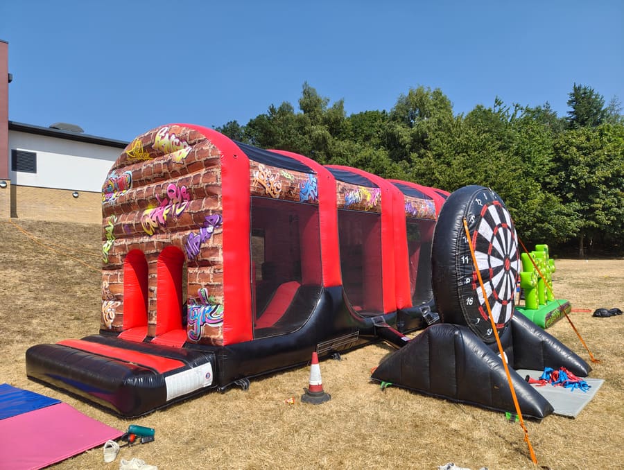 A long inflatable assault course with an arched graffiti-brick entrance, set up on the school field