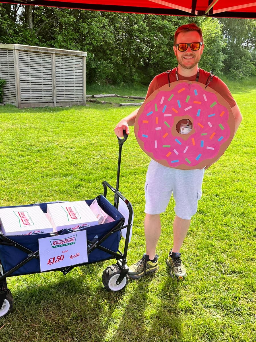 A PSFA volunteer in a homemade cardboard doughnut costume next to a wagon of Krispy Kreme boxes at Sports Day